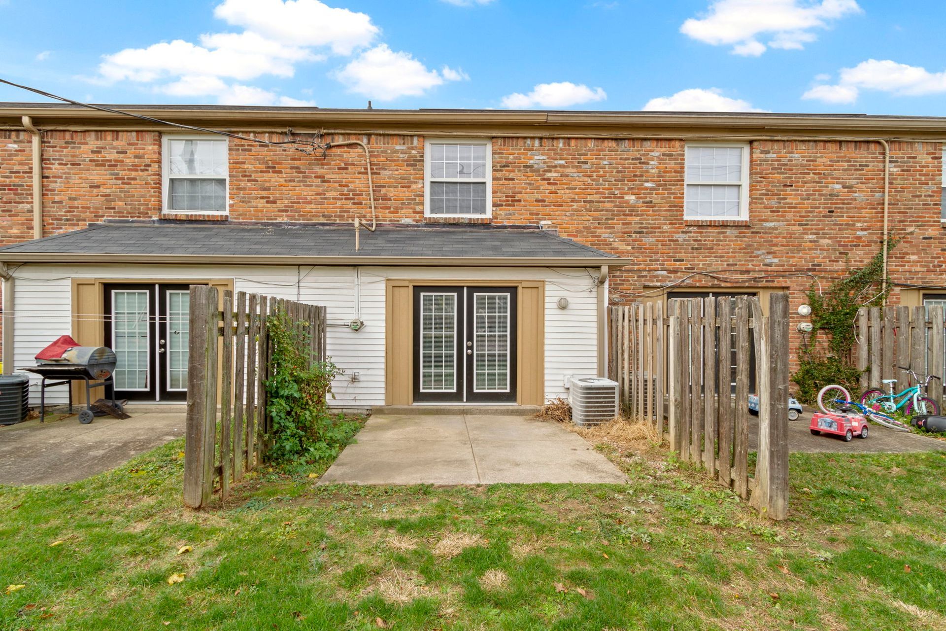 Backyard of a townhome with brick exterior, patio, and wooden fence under a blue sky.
