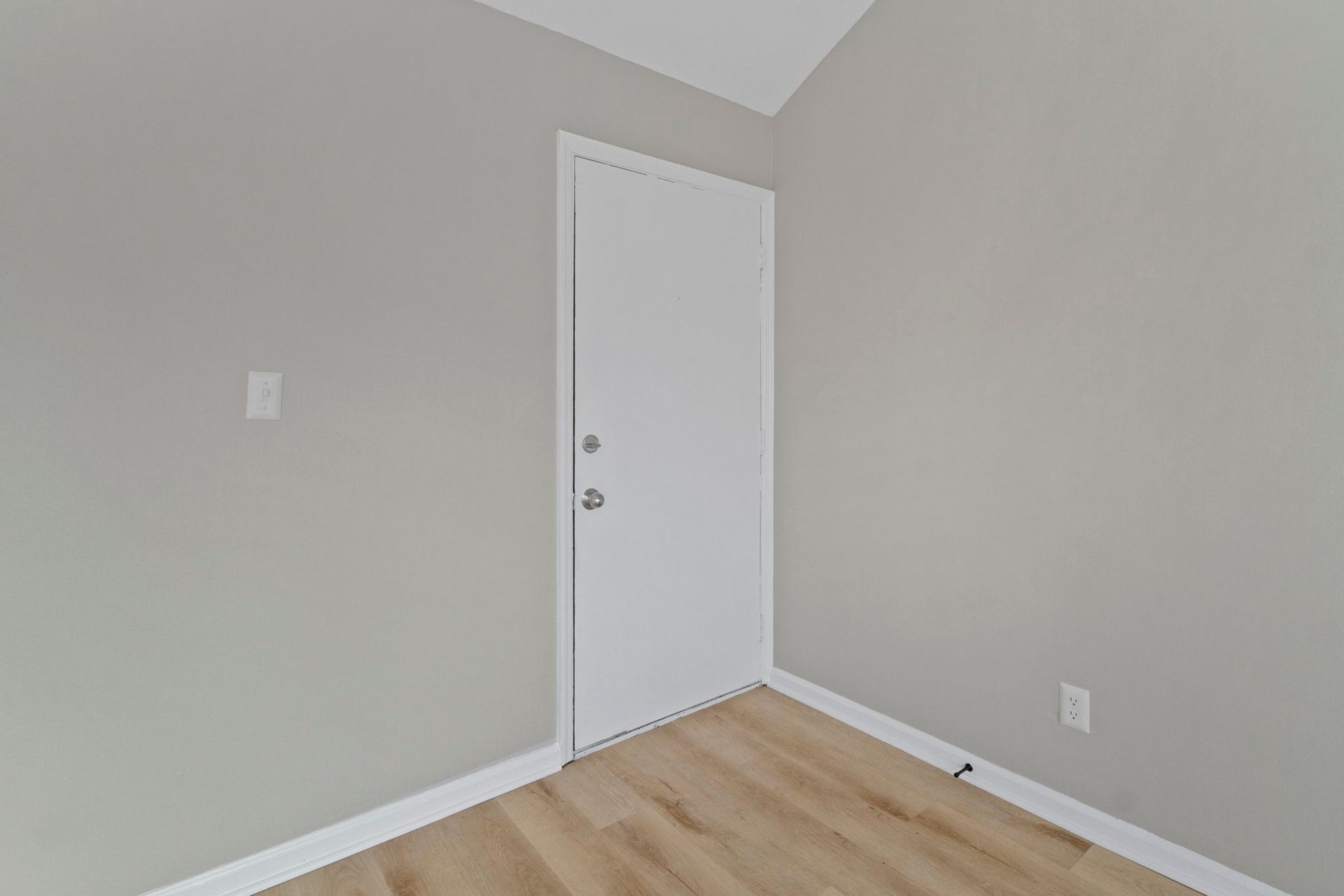 Empty room with a white door and light wood floor. Gray walls and white trim.