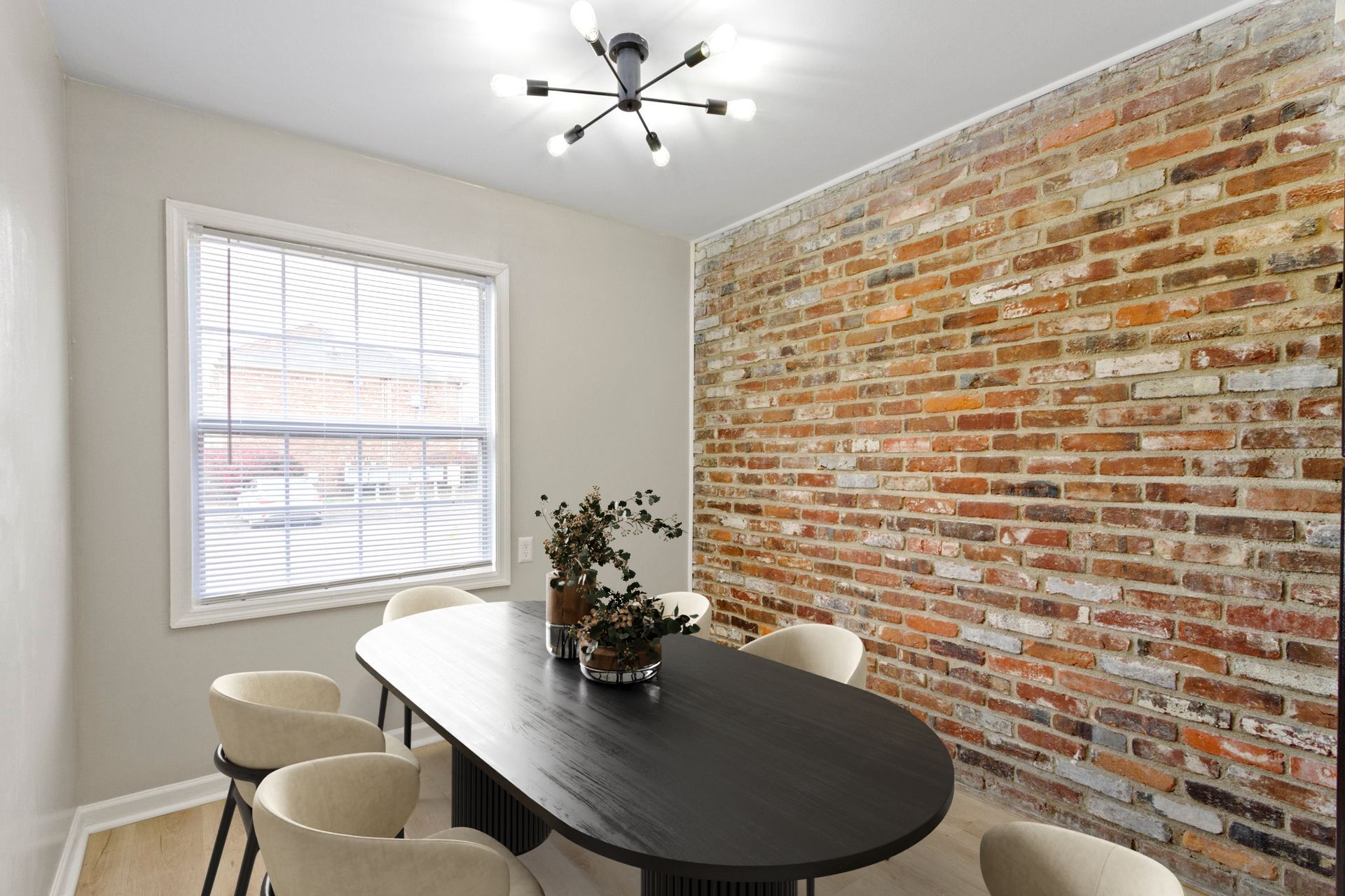 Dining room with oval table, brick wall, and six cream-colored chairs. Ceiling light and window visible.