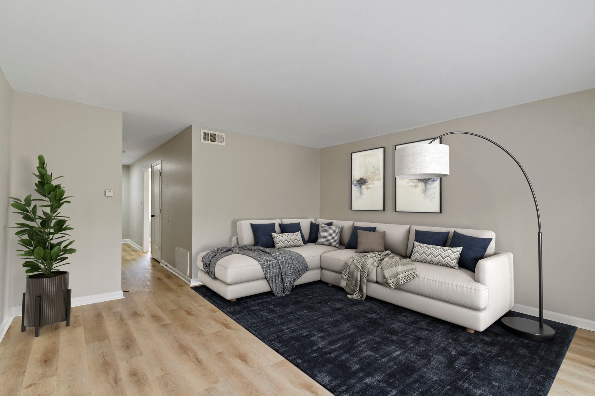 A modern living room with a beige sectional sofa, dark blue rug, and potted plant.