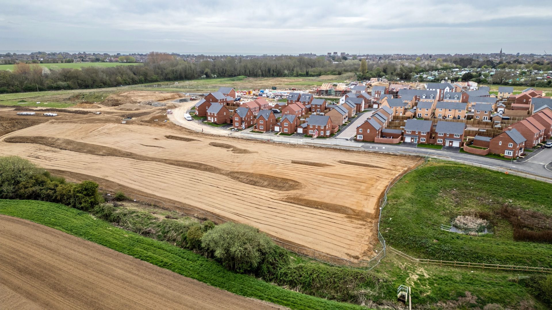 Aerial view of a housing development with new homes, construction in progress, and surrounding fields.