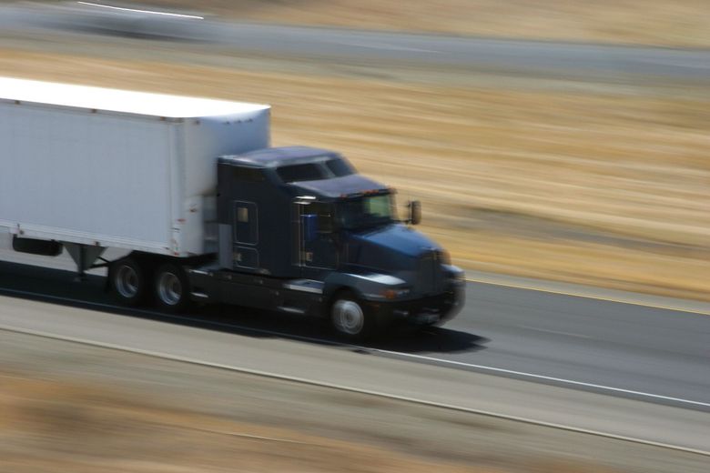 A semi truck with a white trailer is driving down a highway