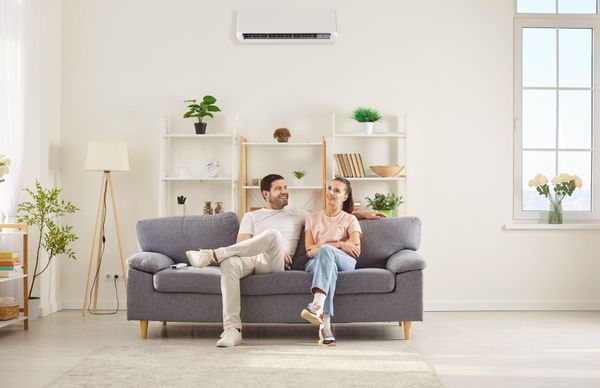 Couple relaxing on a gray sofa in a bright living room with white shelves and plants. Couple relaxing on a gray sofa in a bright living room with white shelves and plants.