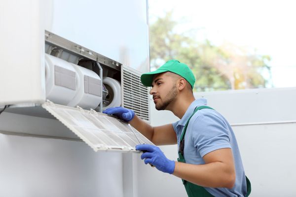 Technician in green cap and gloves cleaning an outdoor air conditioner unit