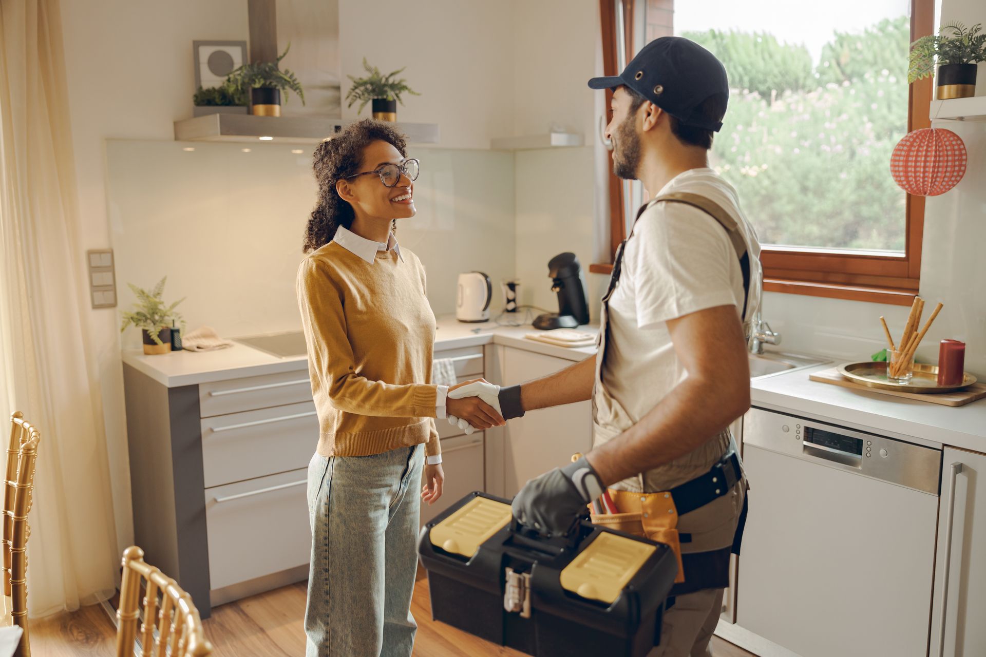 Two people talking in a bright kitchen, one holding an open toolbox and the other gesturing beside the counter.