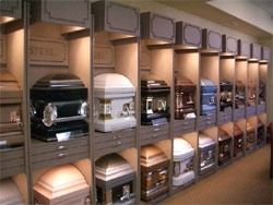Caskets displayed in a showroom; various colors and styles showcased on shelves.