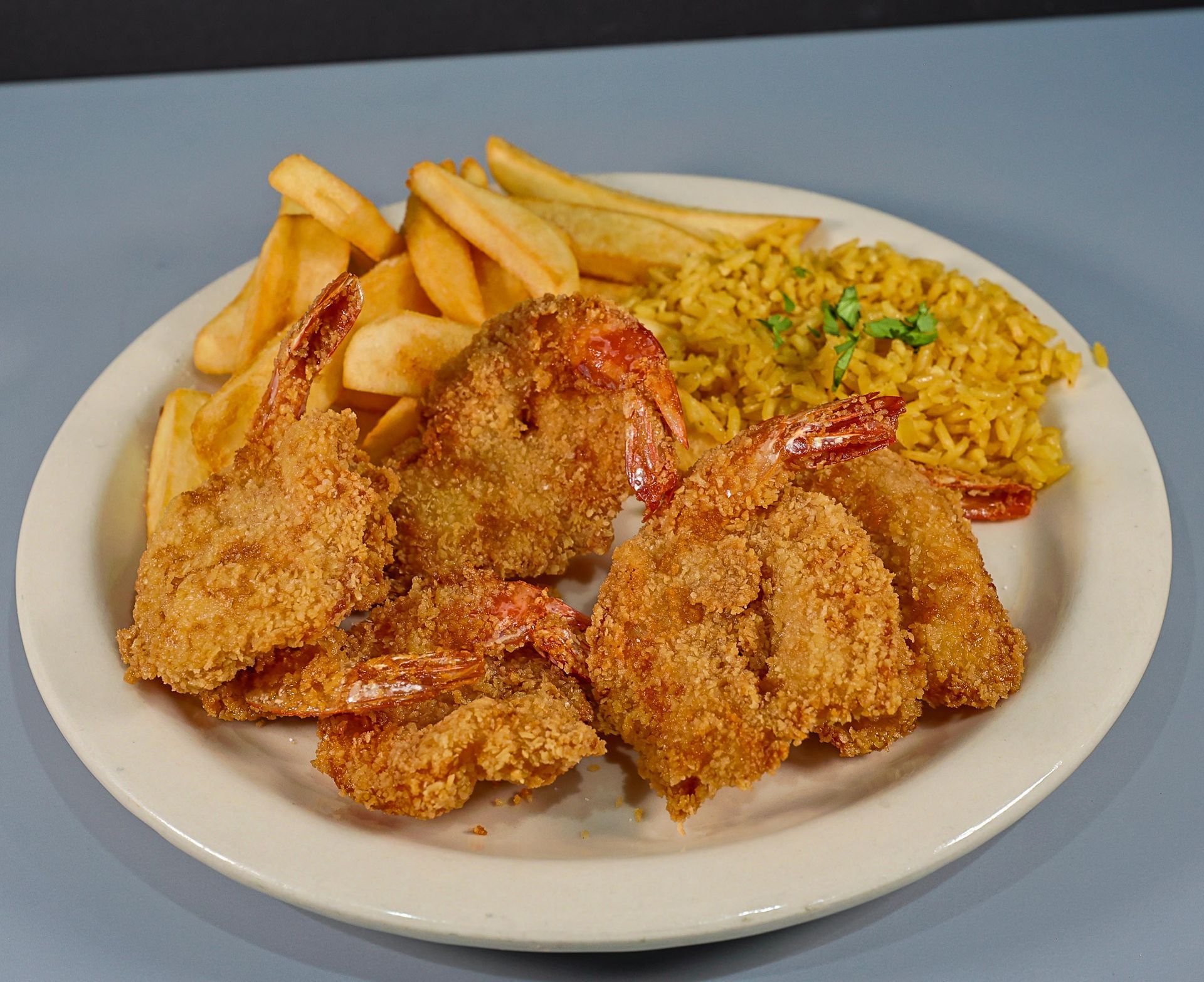 A white plate topped with fried shrimp french fries and rice