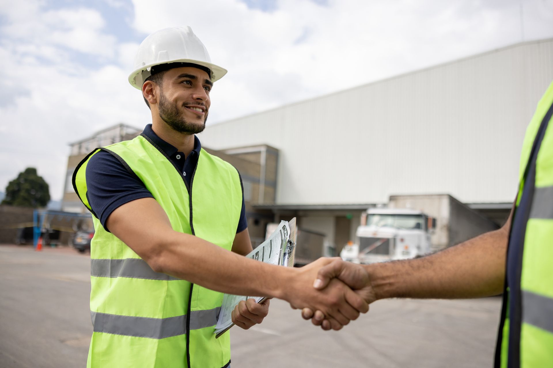 Two men are shaking hands in front of a warehouse.