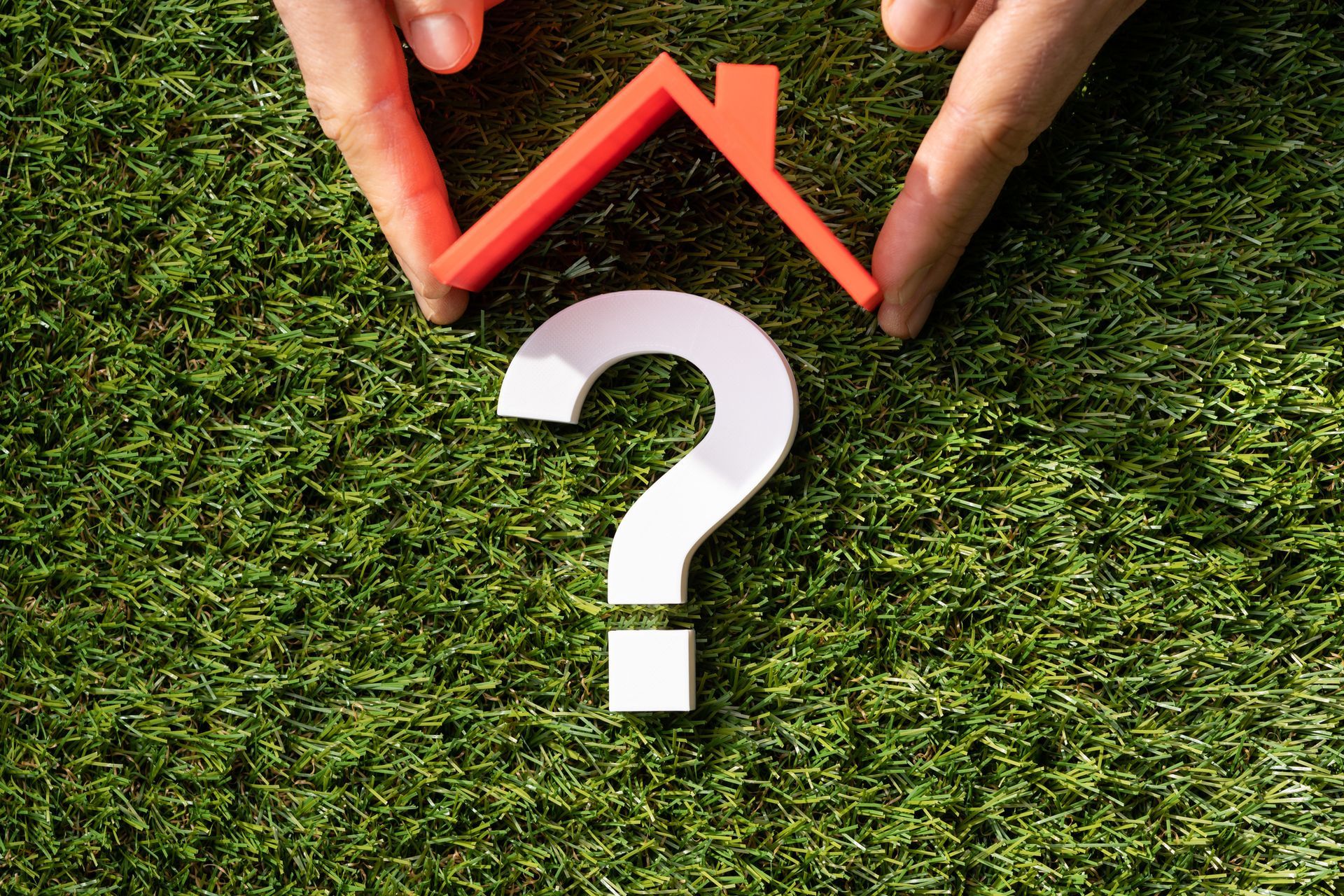 A person is holding a red house and a white question mark on the grass.