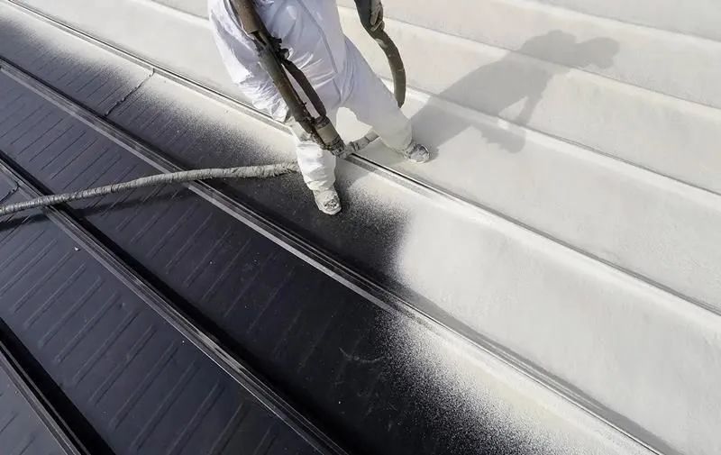 A person is spraying white paint on a roof.