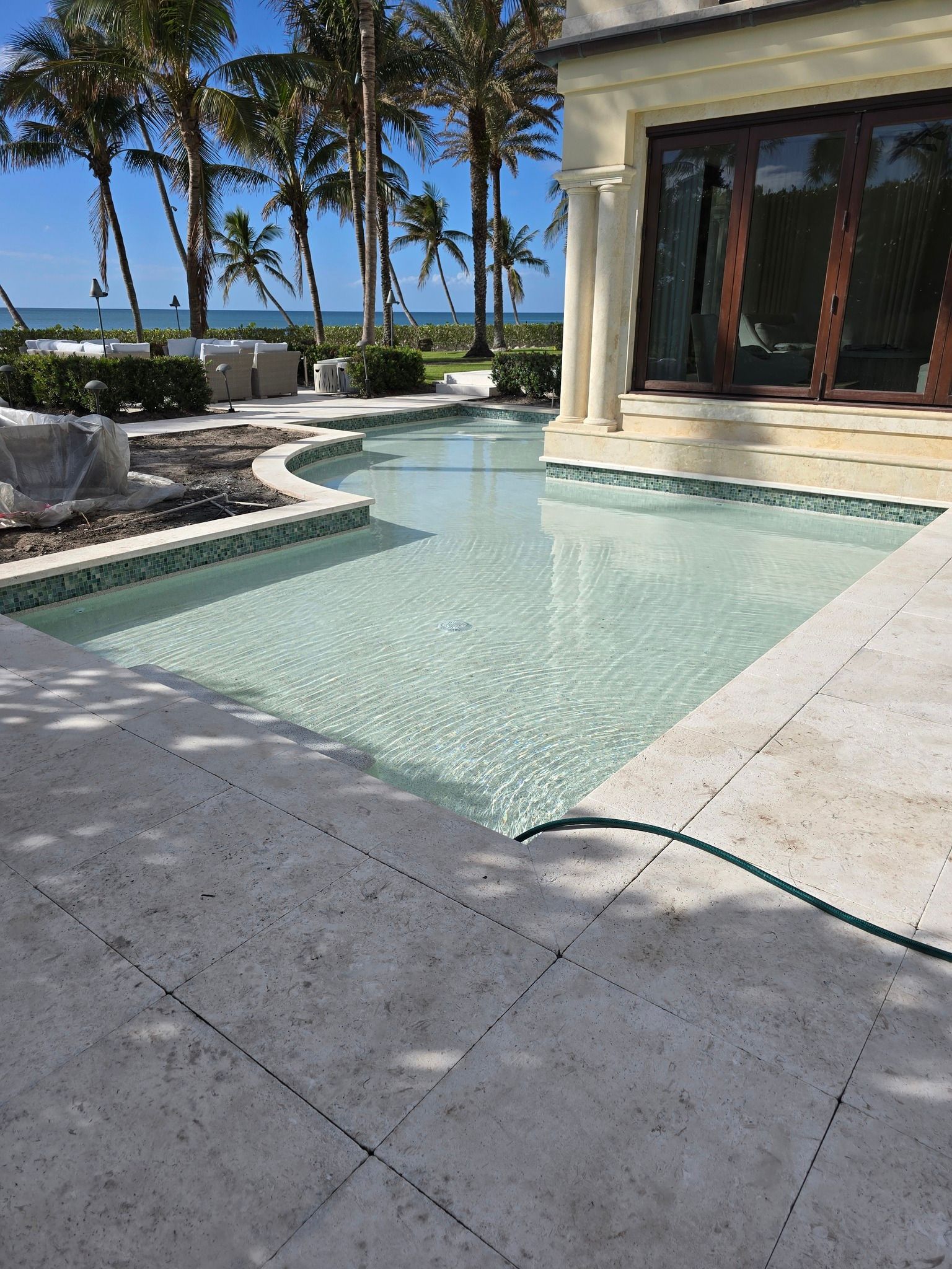 A large swimming pool in front of a house with palm trees in the background.