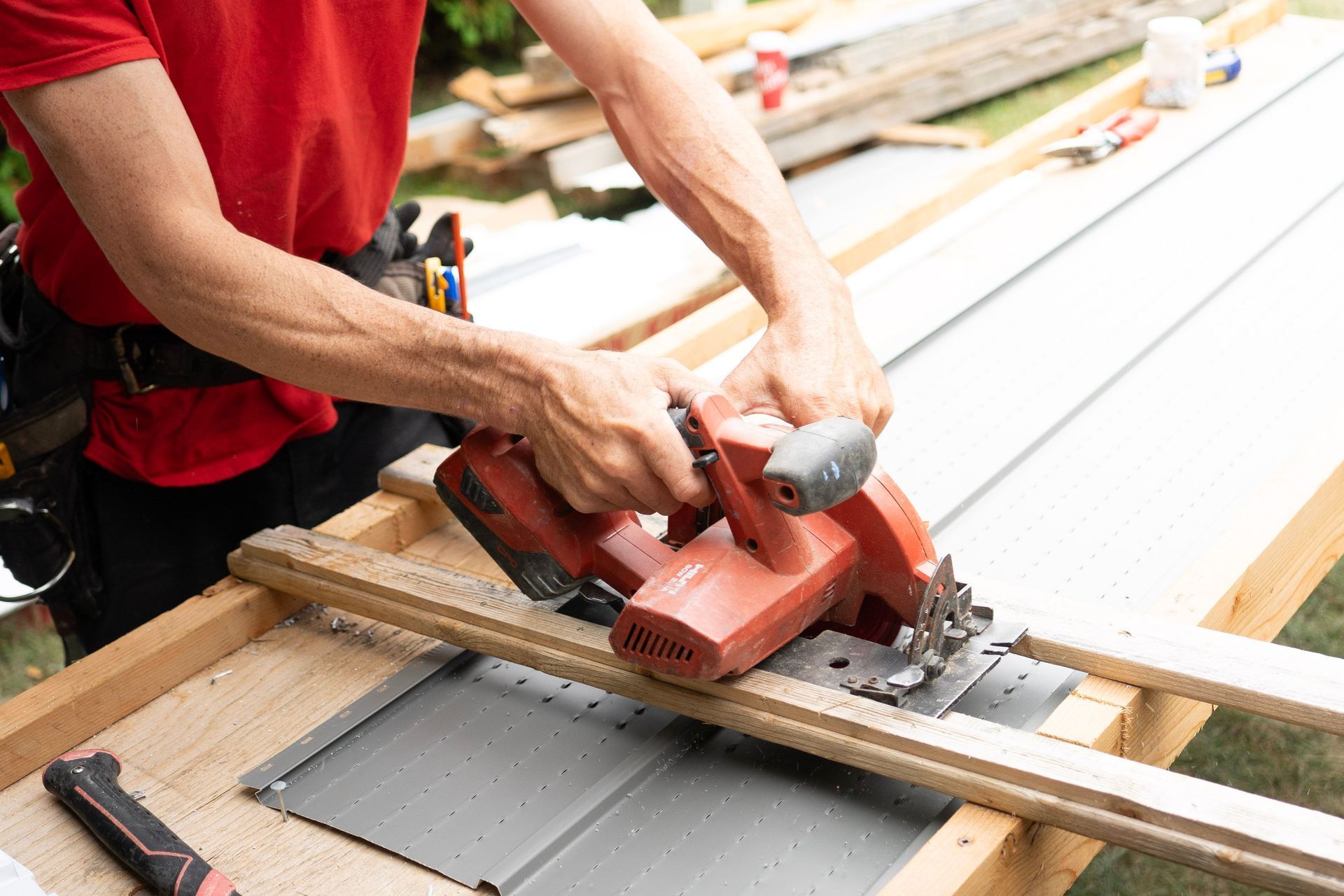 Worker using a red power saw to cut a white board on a workbench
