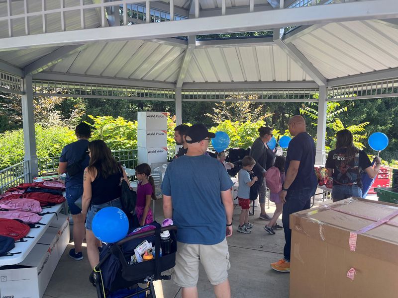 People gather under a gazebo with tables, possibly at an event, some holding blue balloons.