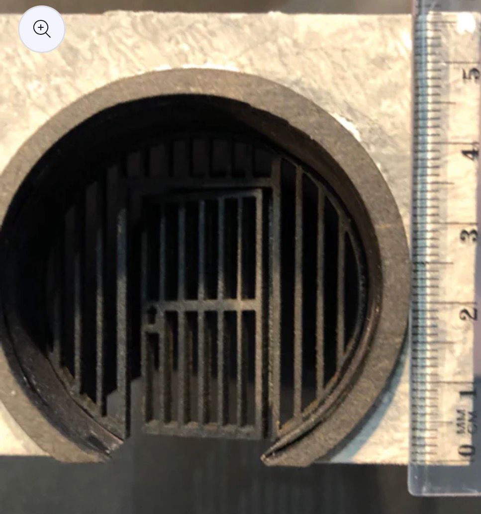 Close-up of a circular opening with a metal gate inside, set in a gray rectangular structure, ruler to the side.