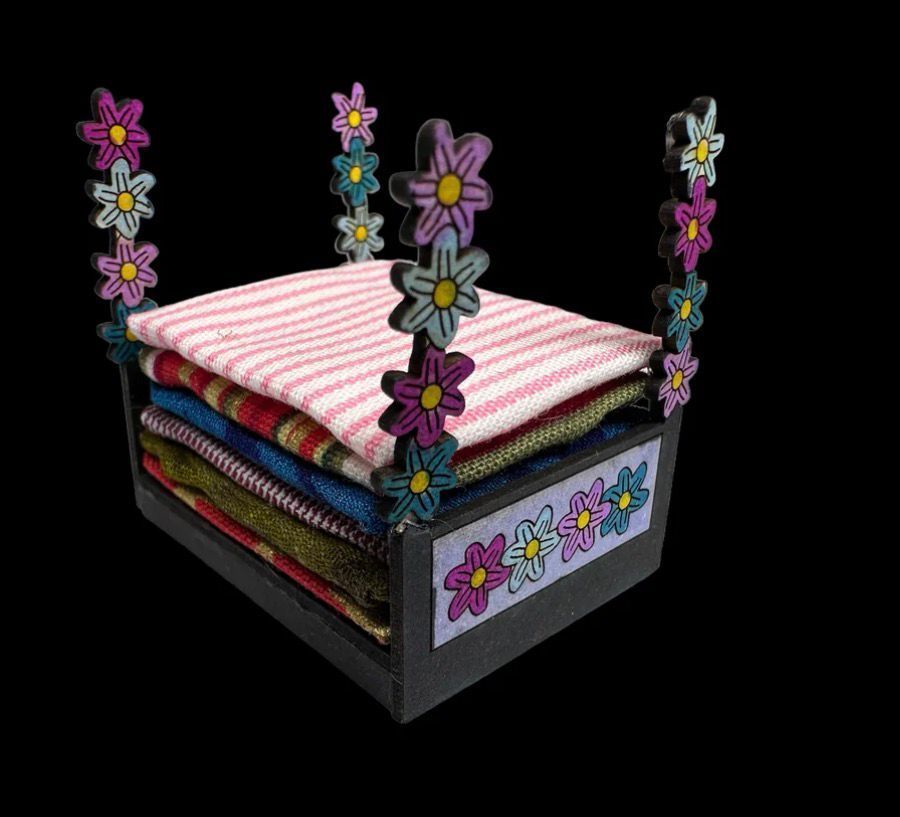 Toy bed made of fabric, with flower details, stacked colorful blankets and pillows.