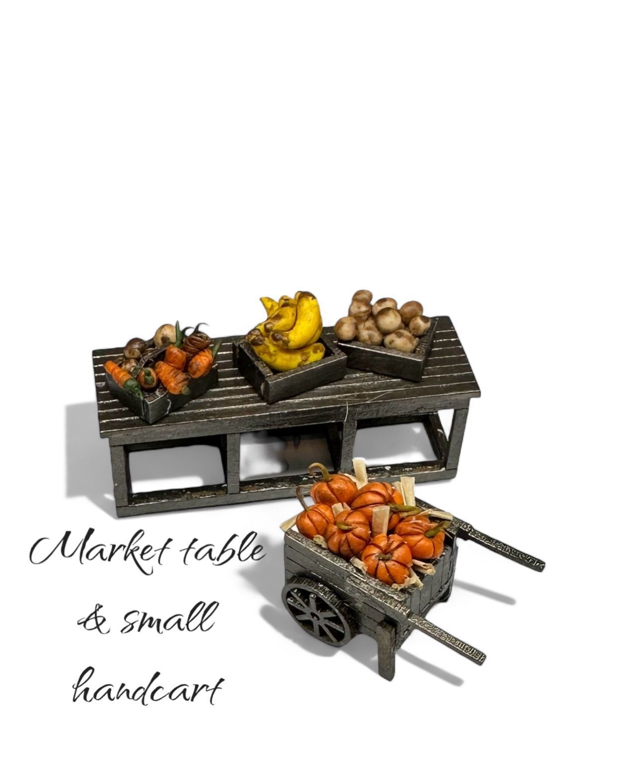 Miniature market scene: produce displayed on a wooden table and handcart. Carrots, bananas, and other items visible.