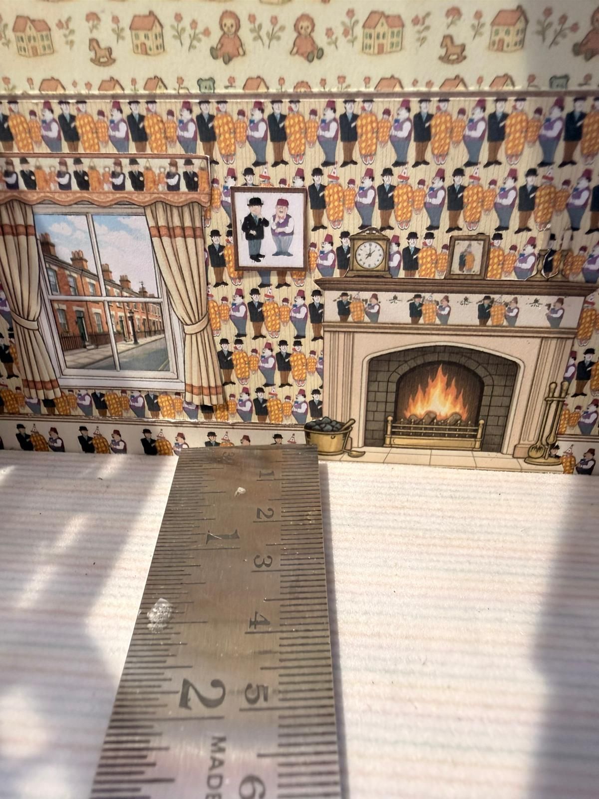 Miniature room scene with wallpaper, fireplace, window, and ruler in foreground.