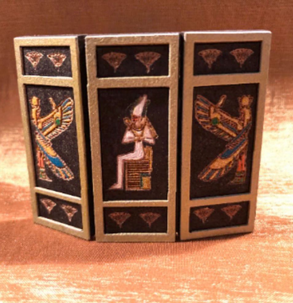 Triptych with Egyptian imagery: figures in gold, black, and tan, with lotus and seated deity on a gold background.