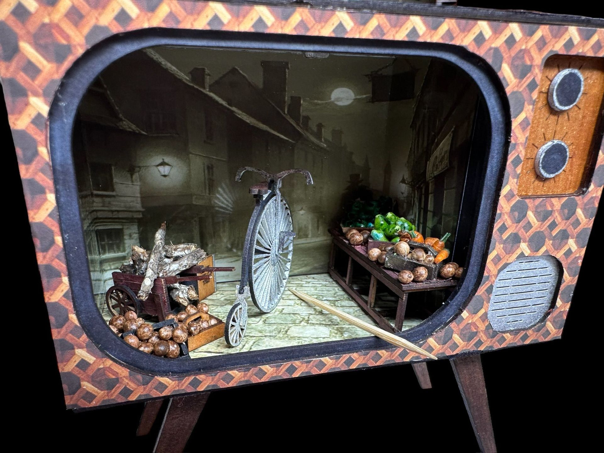 Miniature scene inside a vintage TV. Includes a street setting with bicycle, market, and houses.