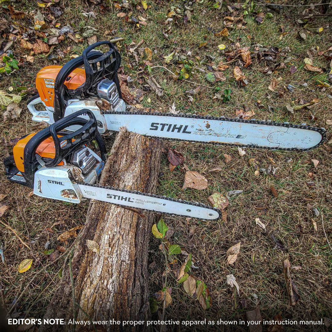 Two Stihl chainsaws on a log in a grassy outdoor setting.