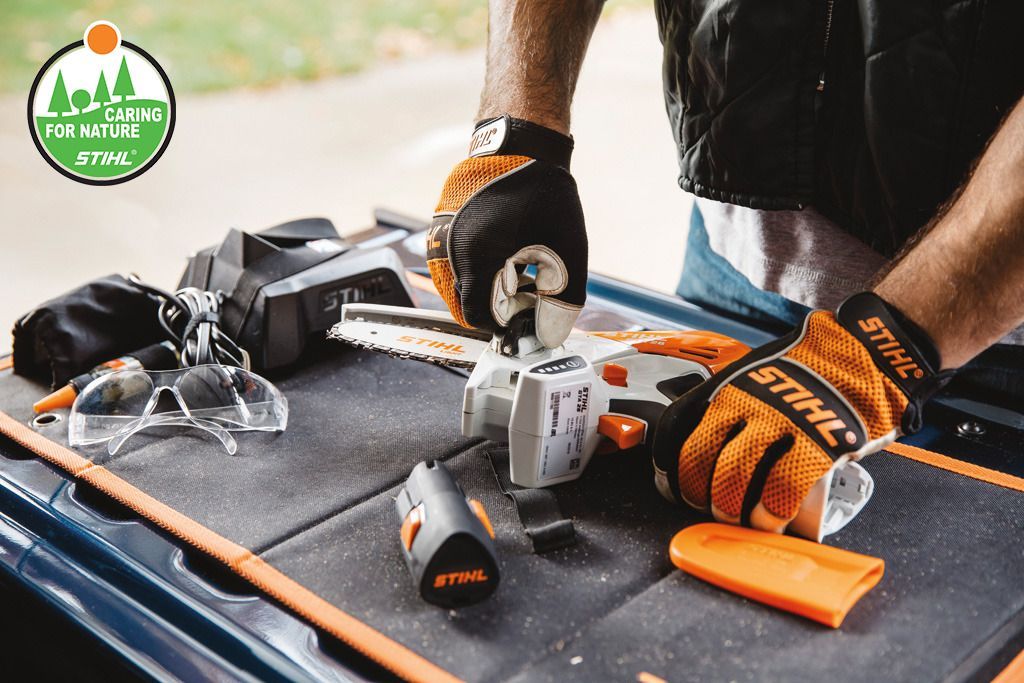 Man wearing orange work gloves using a saw on a workbench; Stihl tools.