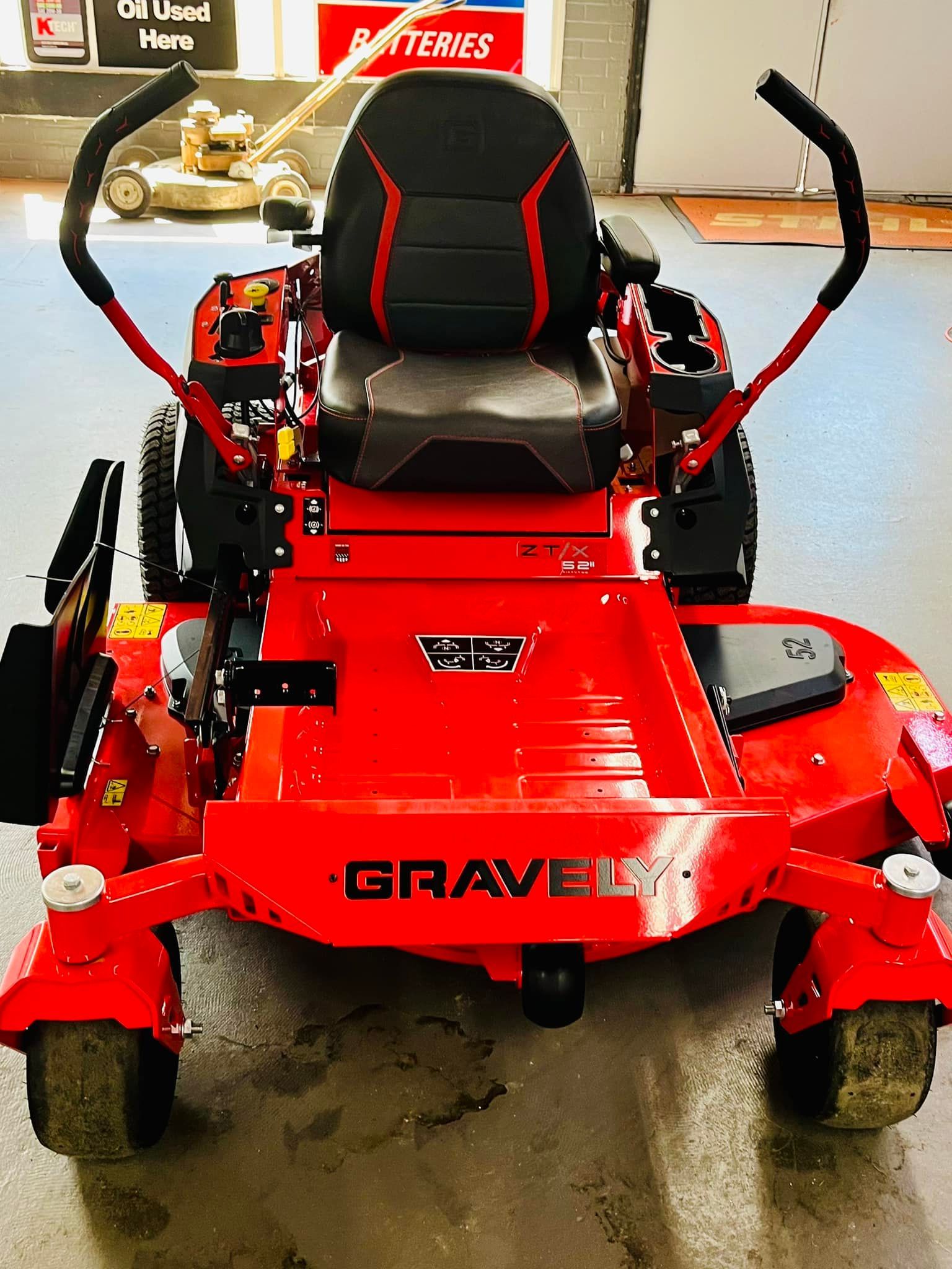 Red Gravely zero-turn lawn mower, black seat with red accents, controls, and a cutting deck, indoors.