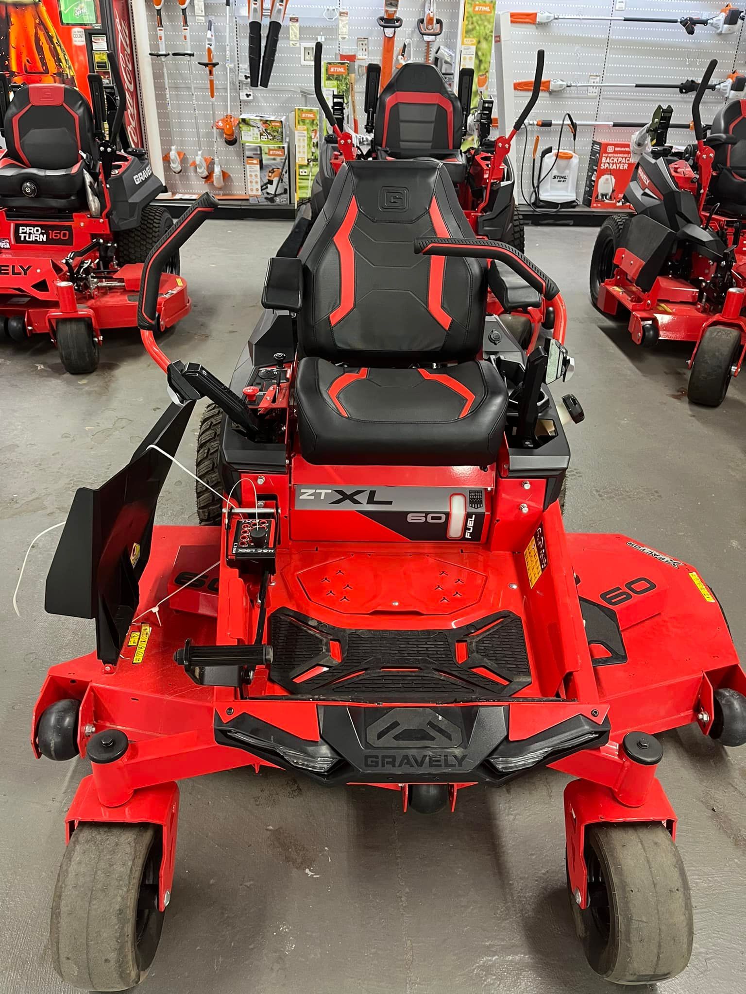 Red Gravely XL zero-turn mower, front view, in a store with other lawn equipment.
