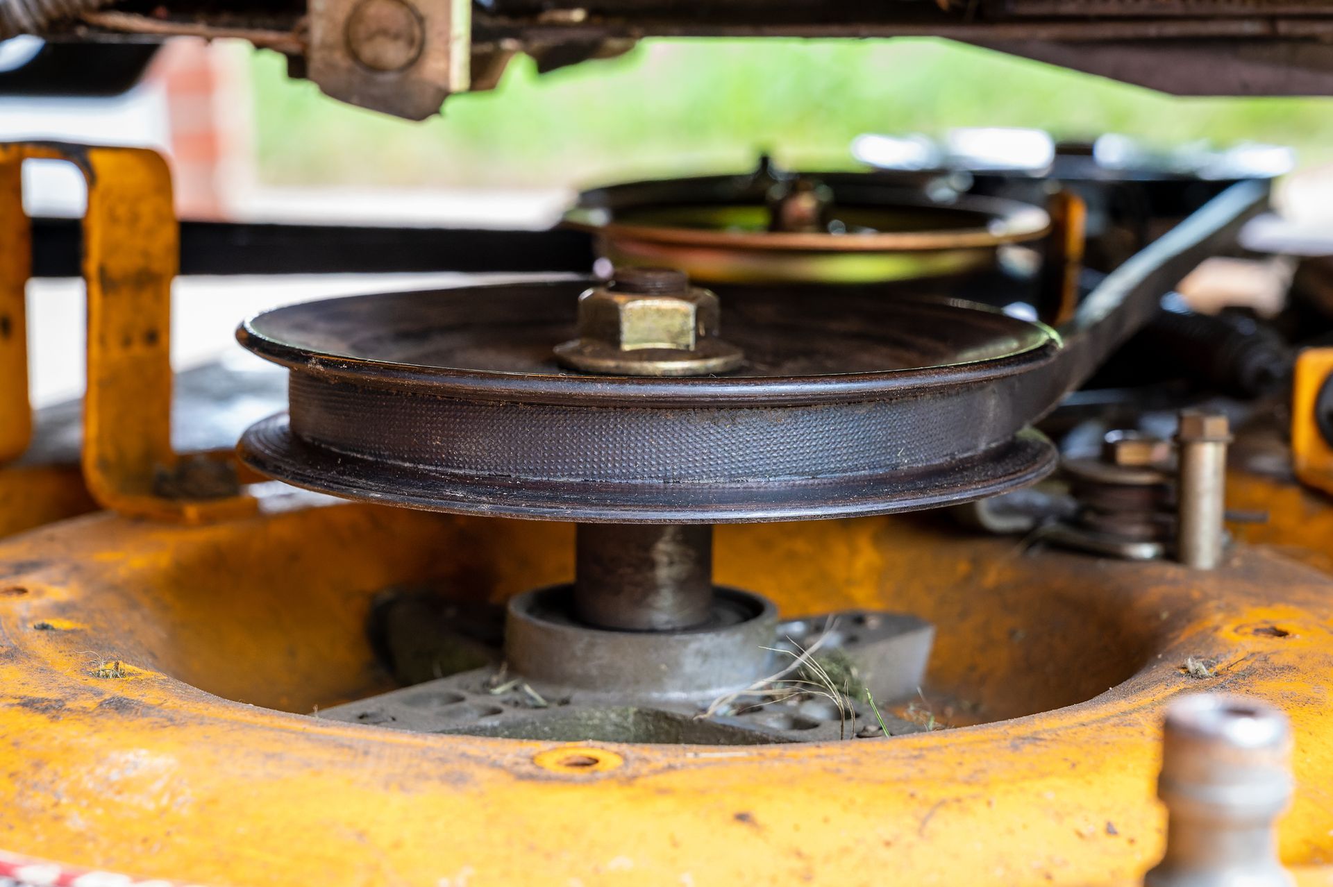 Yellow lawnmower deck with a pulley system and belt, viewed up close.