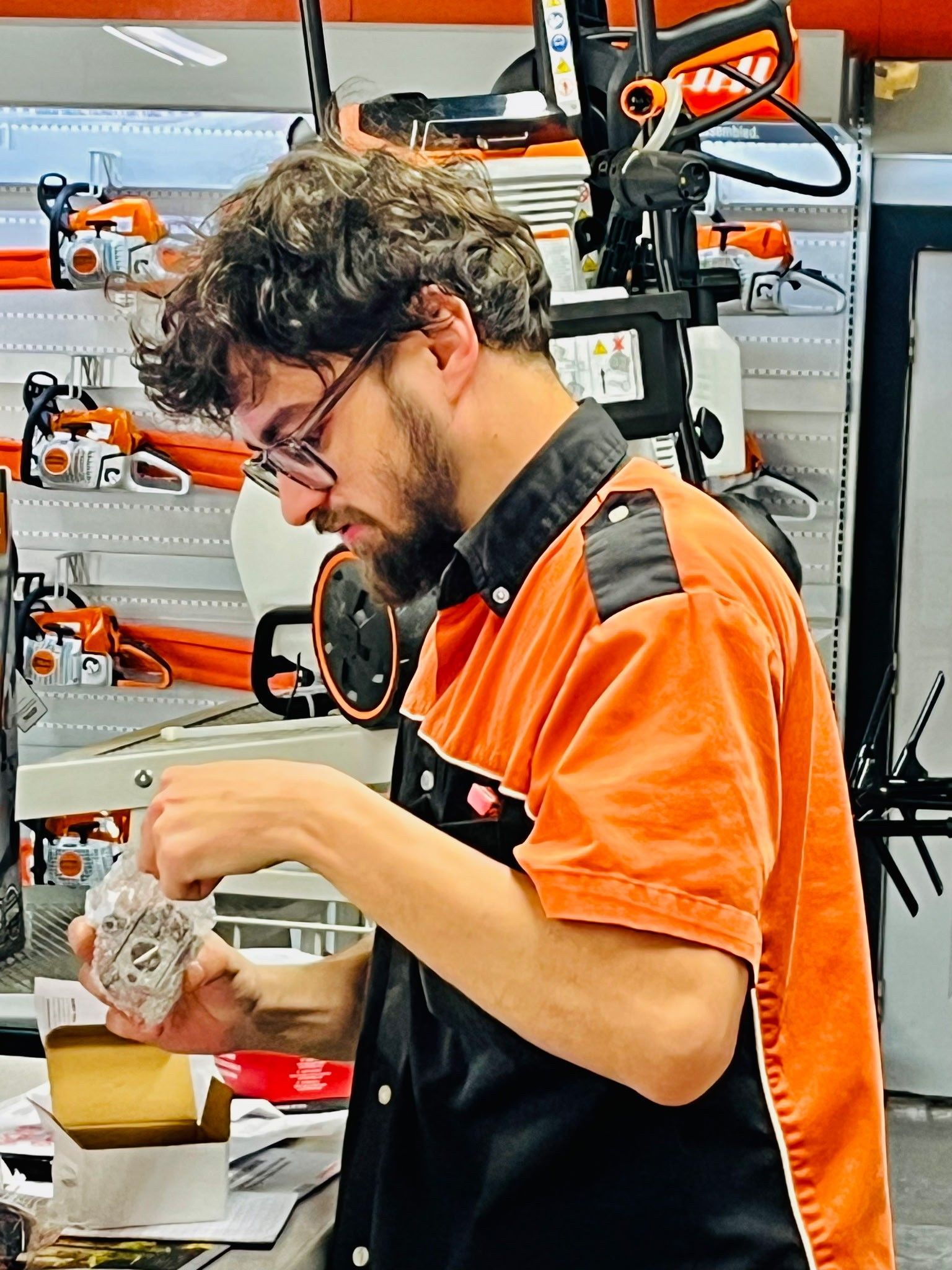 Man unloading a leaf blower from a black pickup truck. Outdoors with a red building in the background.