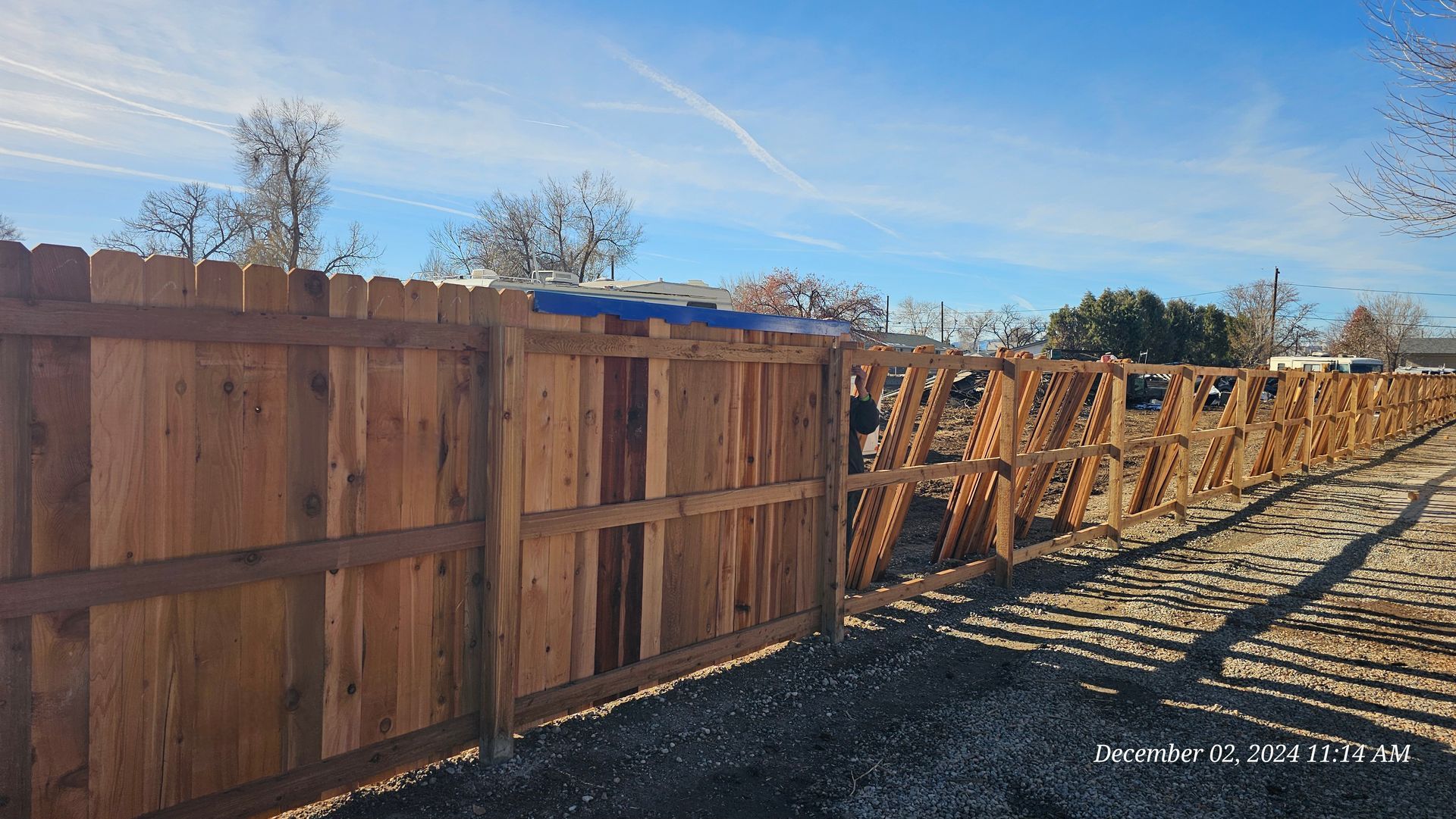A long wooden fence with a solid panel section on the left and a lattice-style section continuing into the distance.