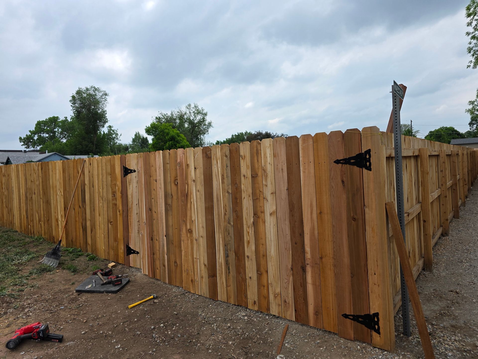 A newly installed wooden fence featuring a gated section with black hinges, positioned on a gravel lot under a cloudy sky.