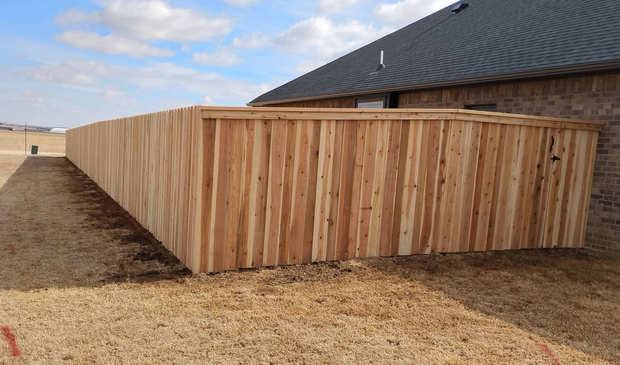 A new wooden fence stands along the side of a brick house in a yard with wood chip mulch.