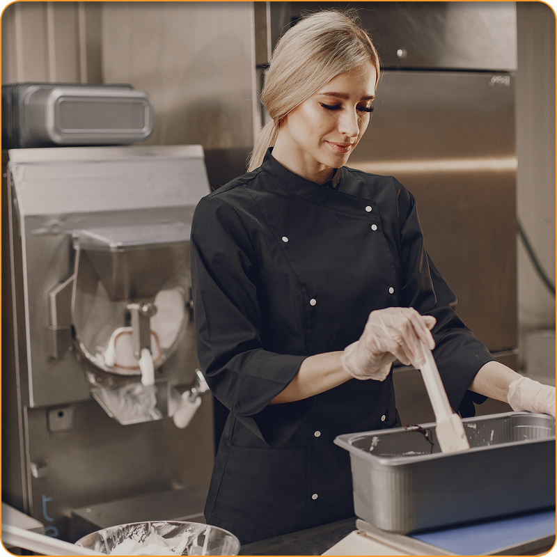 A woman in a black jacket is cooking in a kitchen.