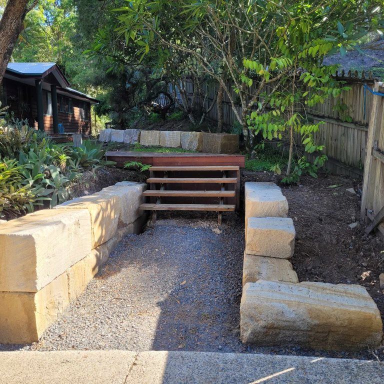 A Stone Wall With Stairs Leading Up to a Wooden Bench in a Garden — Al's Excavation in Bridges, QLD