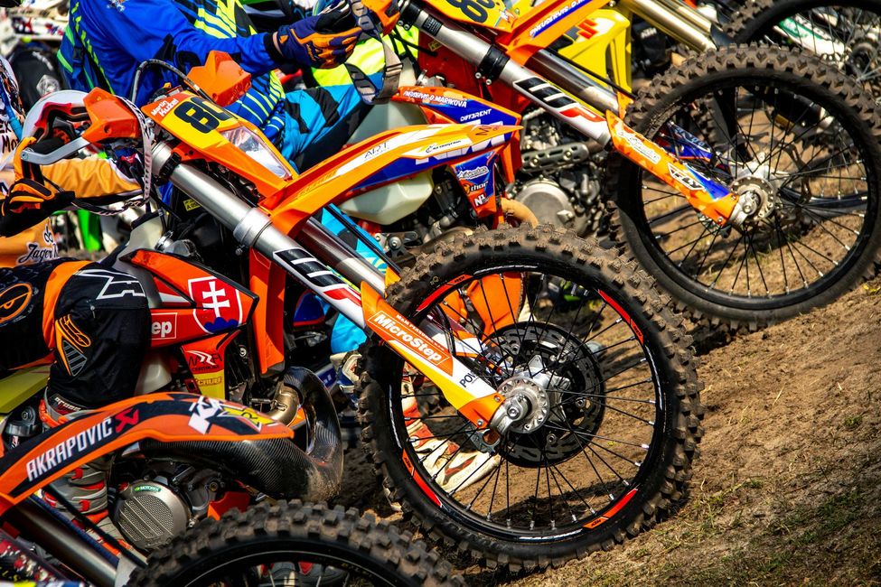 A row of dirt bikes are parked next to each other on a dirt road.