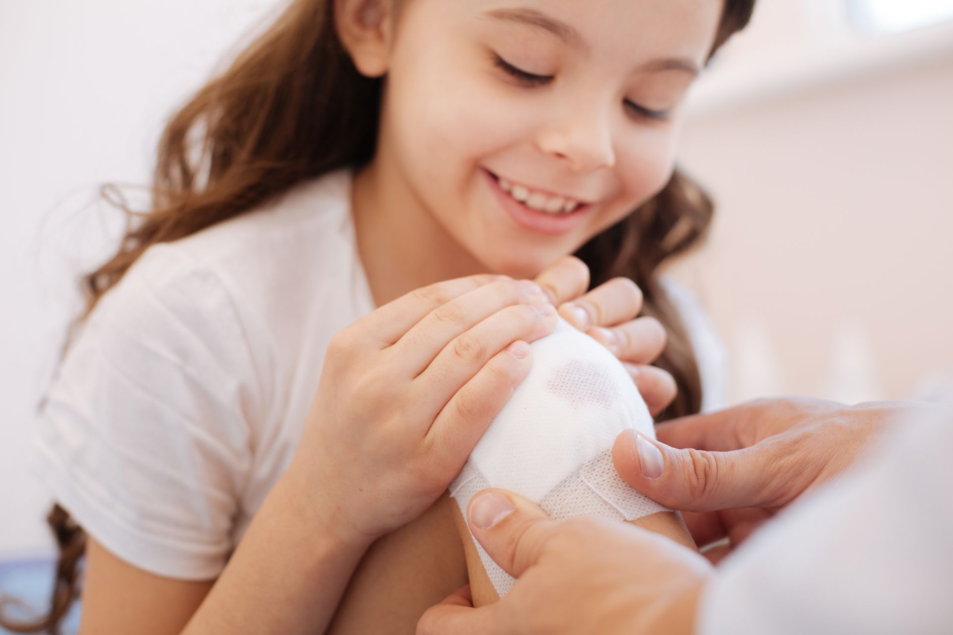 Close-up of a curious girl observing while her doctor performs a wound treatment on her knee. Close-up of a curious girl observing while her doctor performs a wound treatment on her knee.