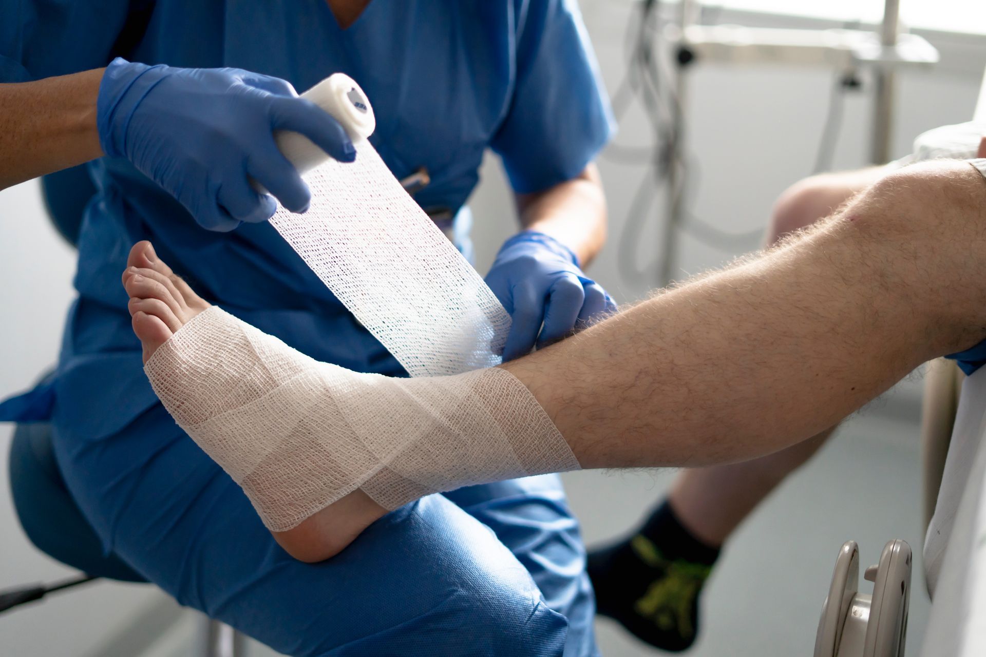 Nurse healing a leg wound in the ankle of a patient sitting on the stretcher with bandages.