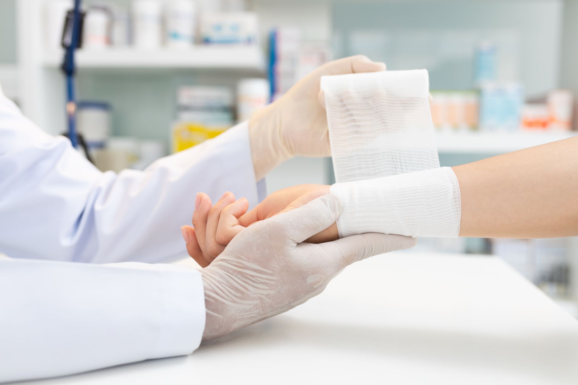 Close-up of a hand wearing medical gloves tying a bandage on the hand of a patient.