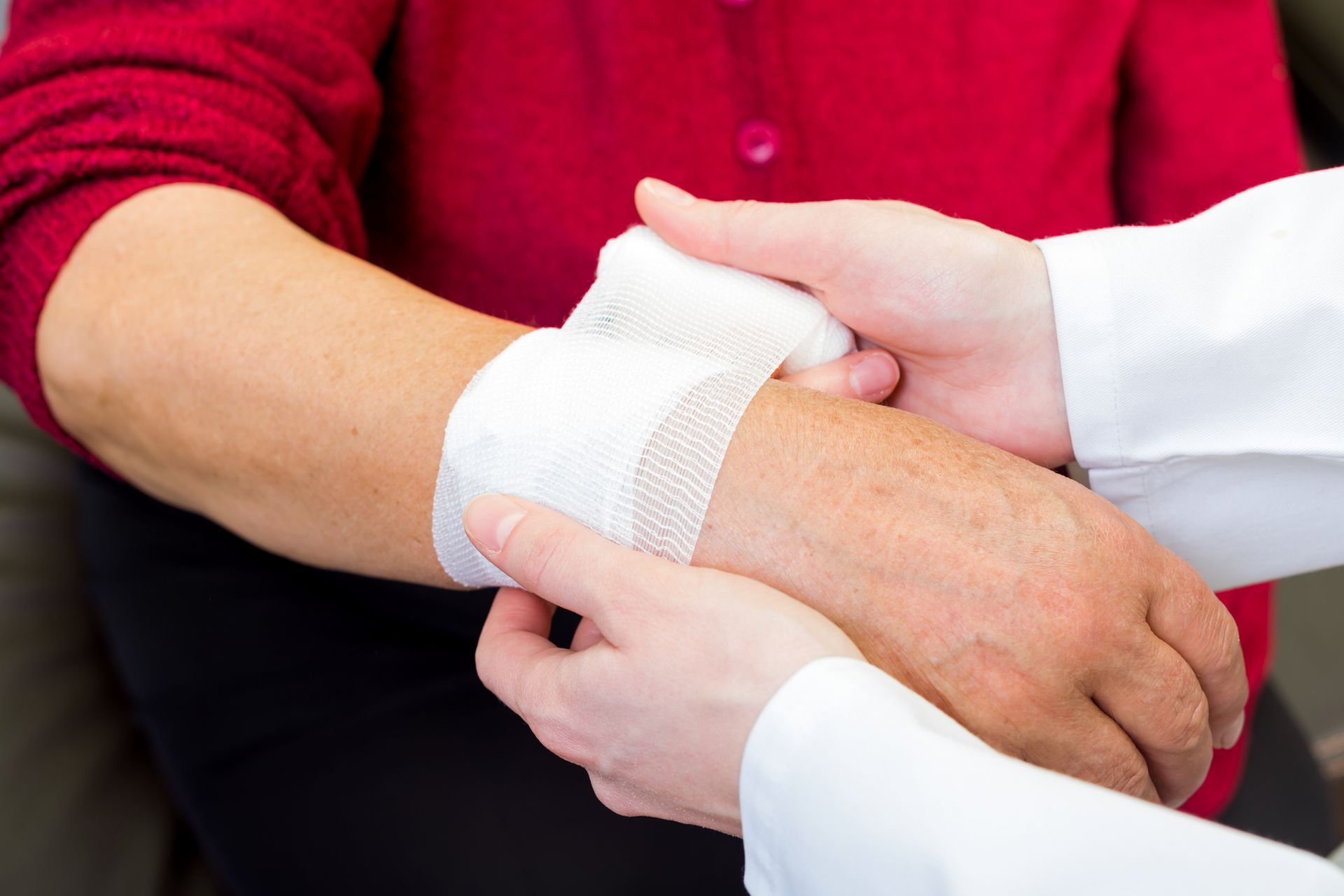 Hands bandaging another's wrist, person wearing red shirt.