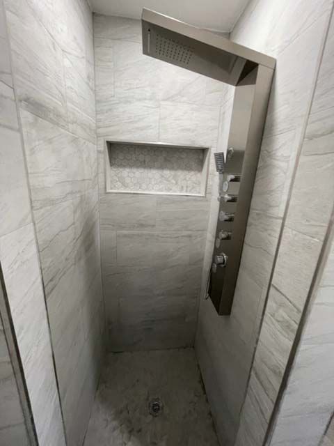 A shower with a stainless steel shower head and a shelf.