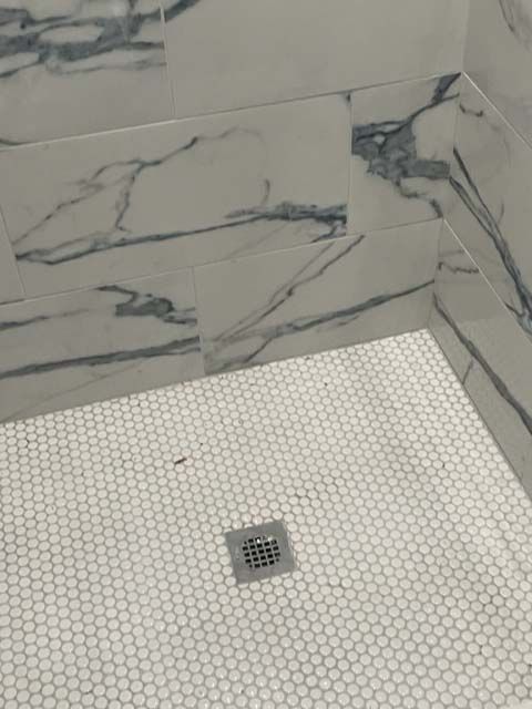 A shower stall with marble tiles and a drain.