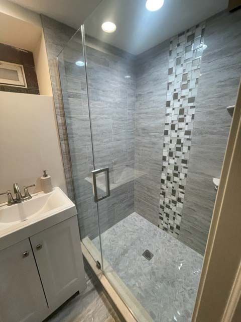 A bathroom with a sink and a walk in shower with a glass door.