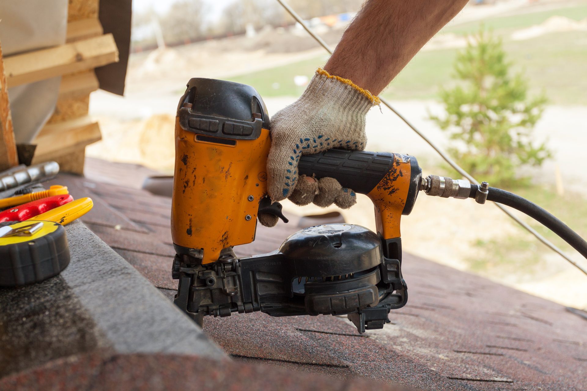Person wearing a glove uses a pneumatic nail gun on a roof.
