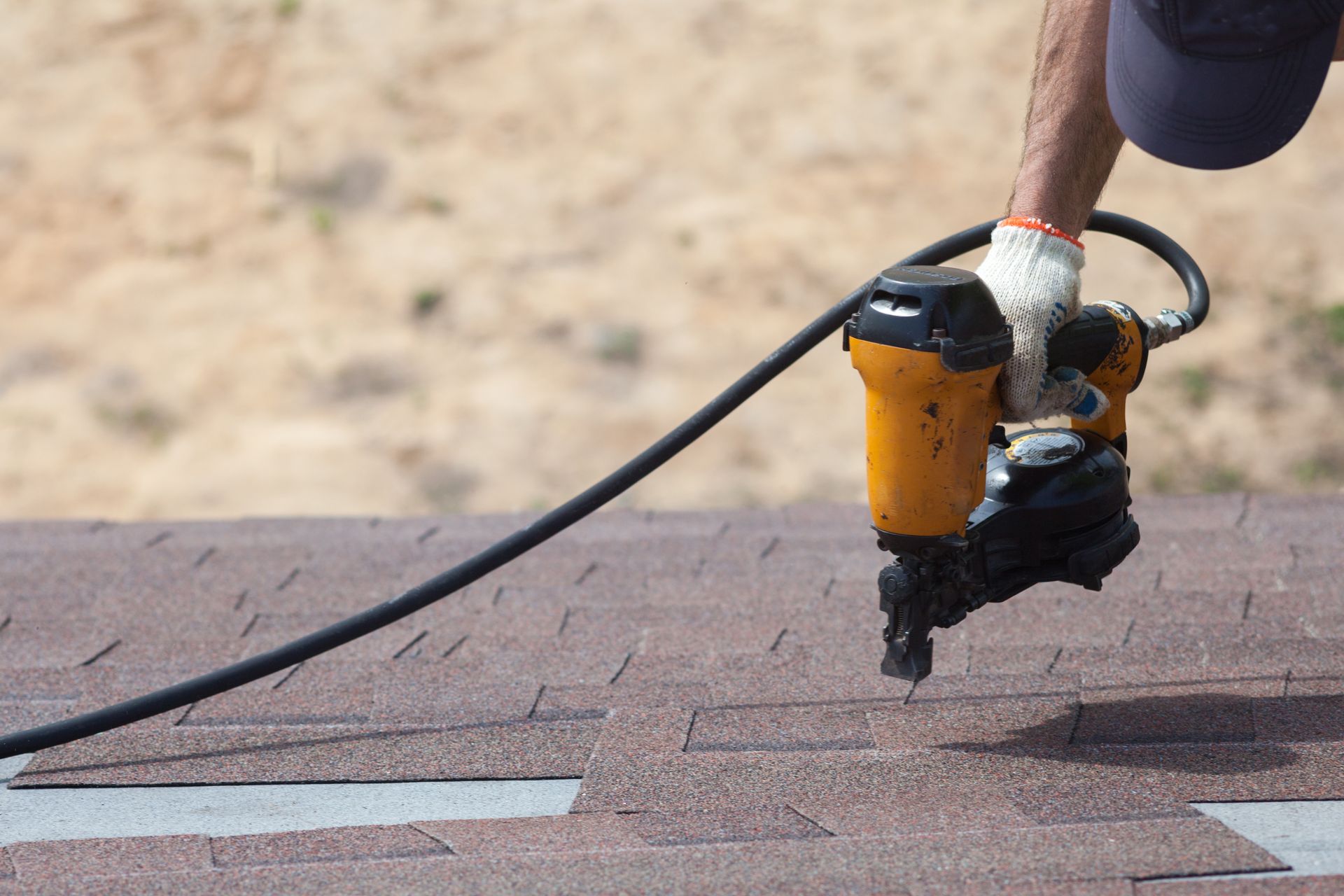 Person using a nail gun to install roofing shingles.