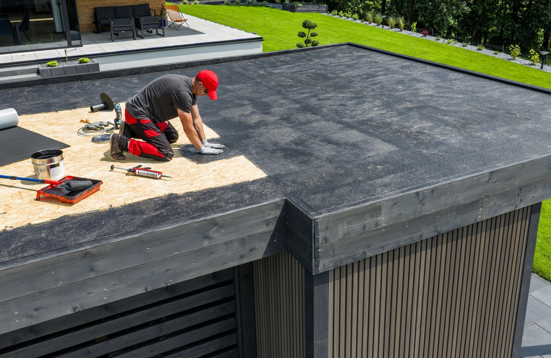 Man in red hat installing roofing on a flat roof, outdoors.