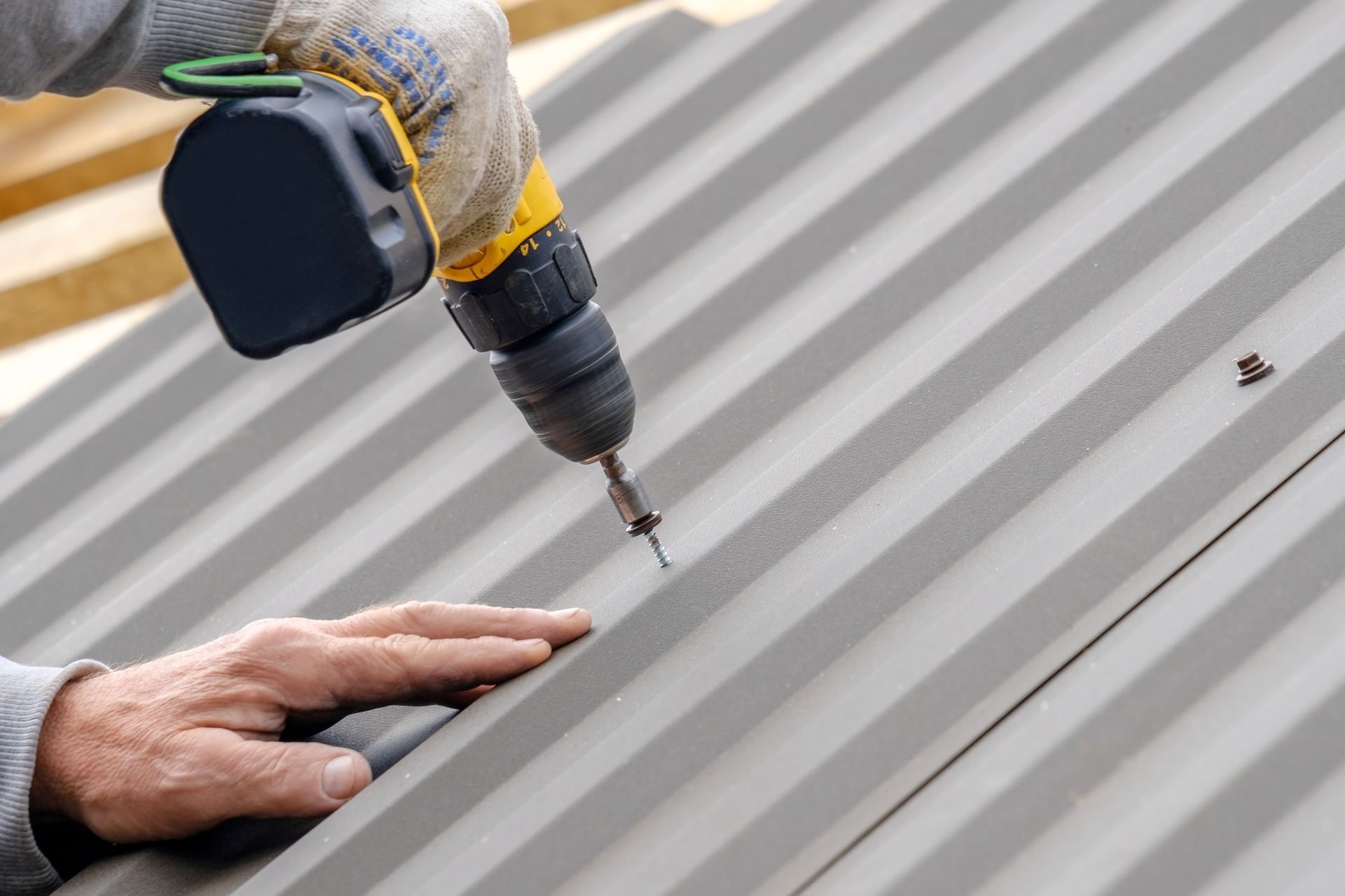 Person using a power drill to install metal roofing.