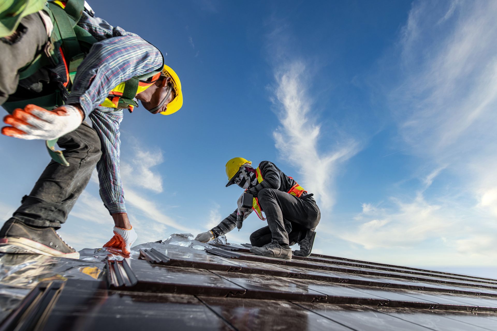 Two workers in safety gear installing solar panels on a rooftop against a blue sky.