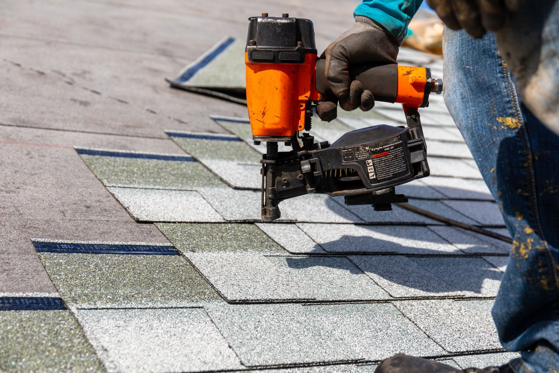 A person using a nail gun to install roofing shingles.
