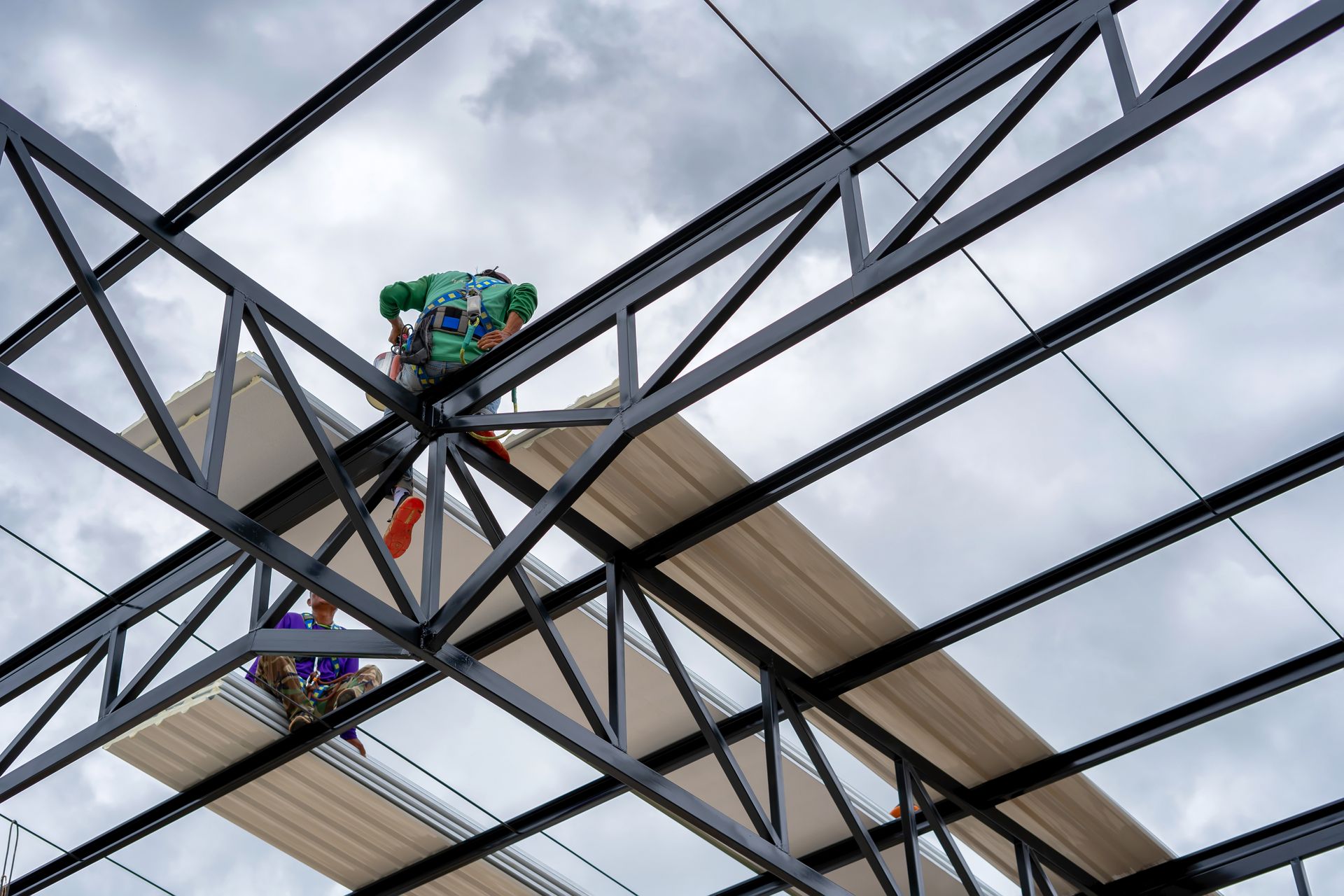 Construction workers installing roofing panels on a steel beam structure under a cloudy sky.