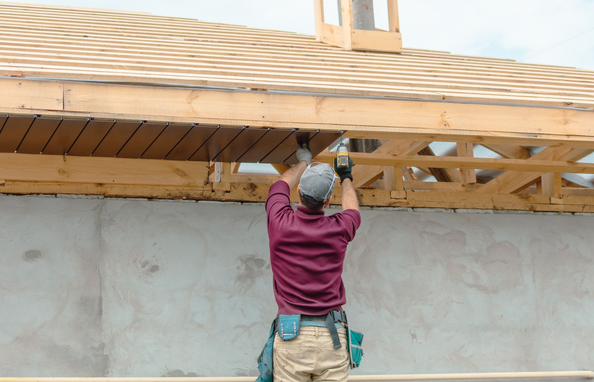 Construction worker on a ladder installing wood paneling under a roof overhang.